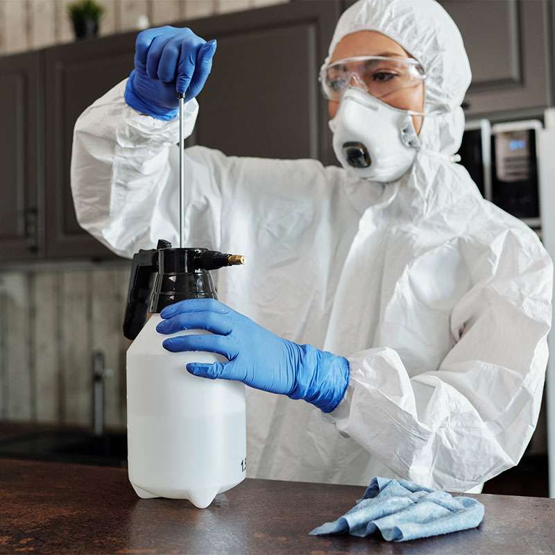 A pest control technician in protective gear preparing a sprayer